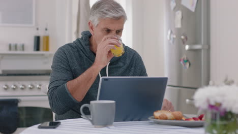 happy-mature-man-using-laptop-computer-at-home-drinking-juice-typing-messages-browsing-online-enjoying-working-in-morning-at-breakfast-4k-footage