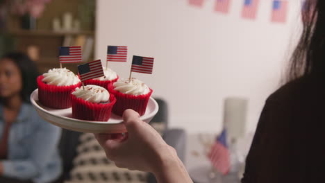 Frau-Zu-Hause-Serviert-Cupcakes-Mit-Miniatur-Amerikanischen-Stars-And-Stripes-Flaggen-An-Freunde-Auf-Party-Feiern-4.-Juli-Unabhängigkeitstag-1