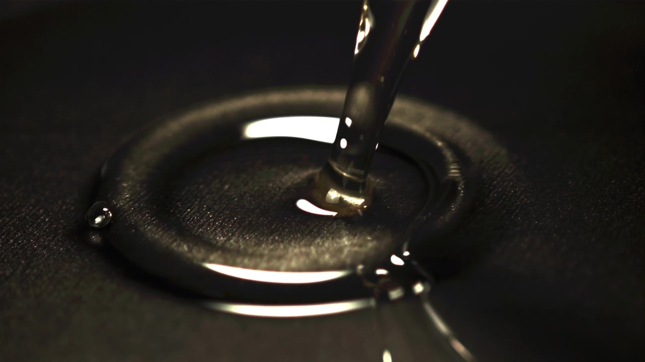 Primer plano de líquido viscoso transparente vertiéndose sobre una superficie oscura