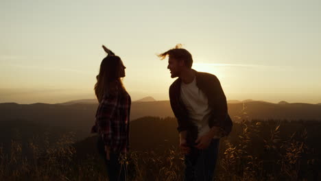 mujer y hombre sonrientes bailando juntos en la cima de la montaña al atardecer