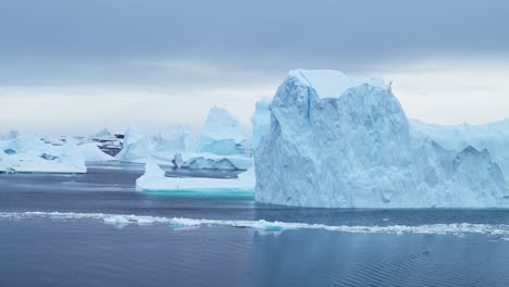 Gran-Puesta-De-Sol-Del-Paisaje-Del-Iceberg-De-La-Antártida,-Grandes-Icebergs-Azules-Masivos-Con-Formas-Asombrosas-Y-Nubes-Dramáticas-Y-Cielo-En-El-Paisaje-Marino-Invernal-Del-Amanecer-En-La-Península-Antártica-En-Una-Escena-Helada