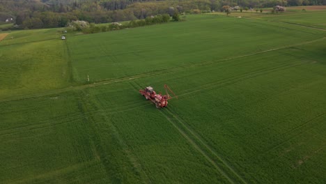 aerial footage of a tractor unfolding its sprinkler system in a huge green meadow