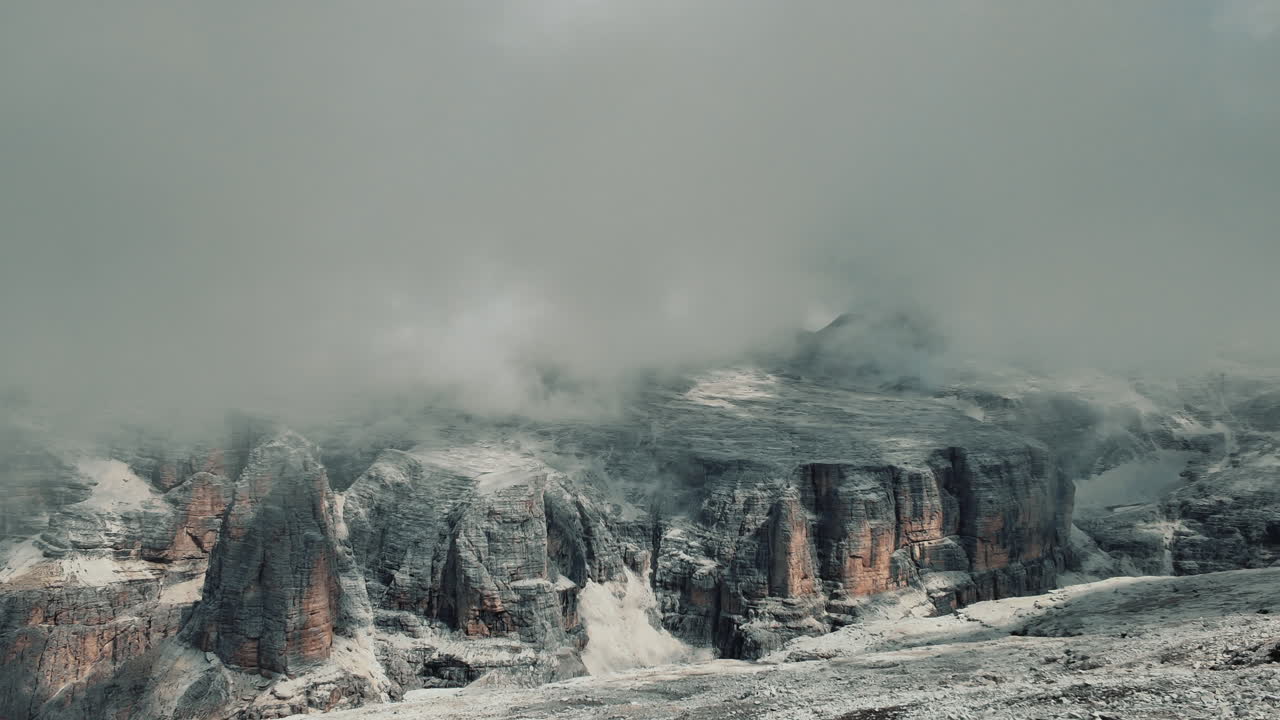 Dramatic cloudscape rolling over rocky Dolomite peaks at Pordoi Pass, capturing mesmerizing mountain landscape transforming through time and light