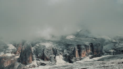 dramatic cloudscape rolling over rocky dolomite peaks at pordoi pass, capturing mesmerizing mountain landscape transforming through time and light