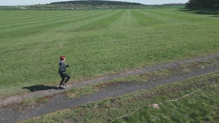 Ripresa dinamica con drone di una donna che fa jogging lungo una strada sterrata in un vasto paesaggio
