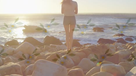 Animation-of-floral-pattern-over-woman-by-seaside