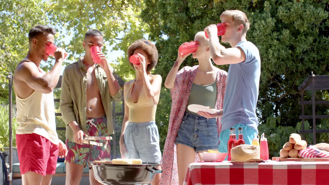 Blije diverse groep vrienden die drankjes drinkt en barbecueën in de tuin in de zomer