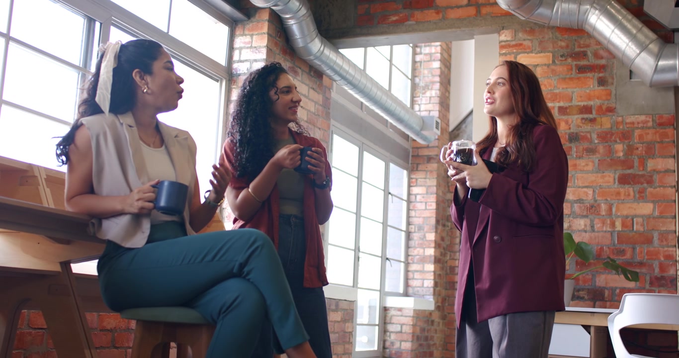 Diverse team taking break near windows, holding mugs while right woman showing camera and sipping
