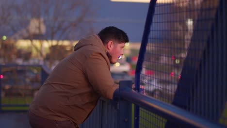 a medium shot of a man standing on a blue iron bridge, gazing into the distance with cars passing by in the blurred background. slow-motion footage capturing a reflective, cinematic moment.