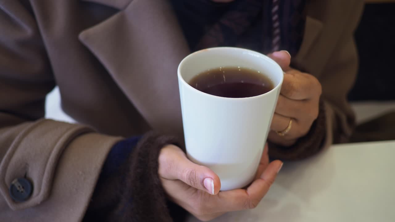 Person's Hands Holding and Sipping from a White Mug