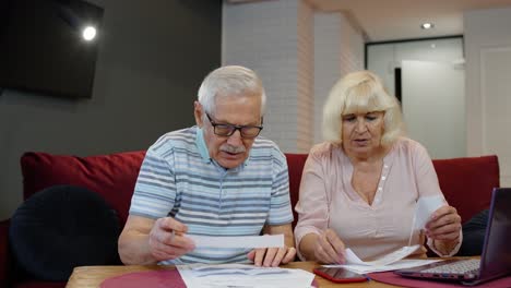 Senior-couple-checking-calculating-bills-bank-loan-payment-doing-paperwork-discuss-unpaid-debt-taxes