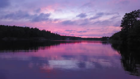 aerial drone shot close to the water, above a lake and towards the forest, a purple sky, at a colorful sunset or dusk, at albysjon, tyreso, sweden