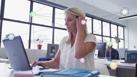 animation of network of digital icons over caucasian woman using a laptop at office