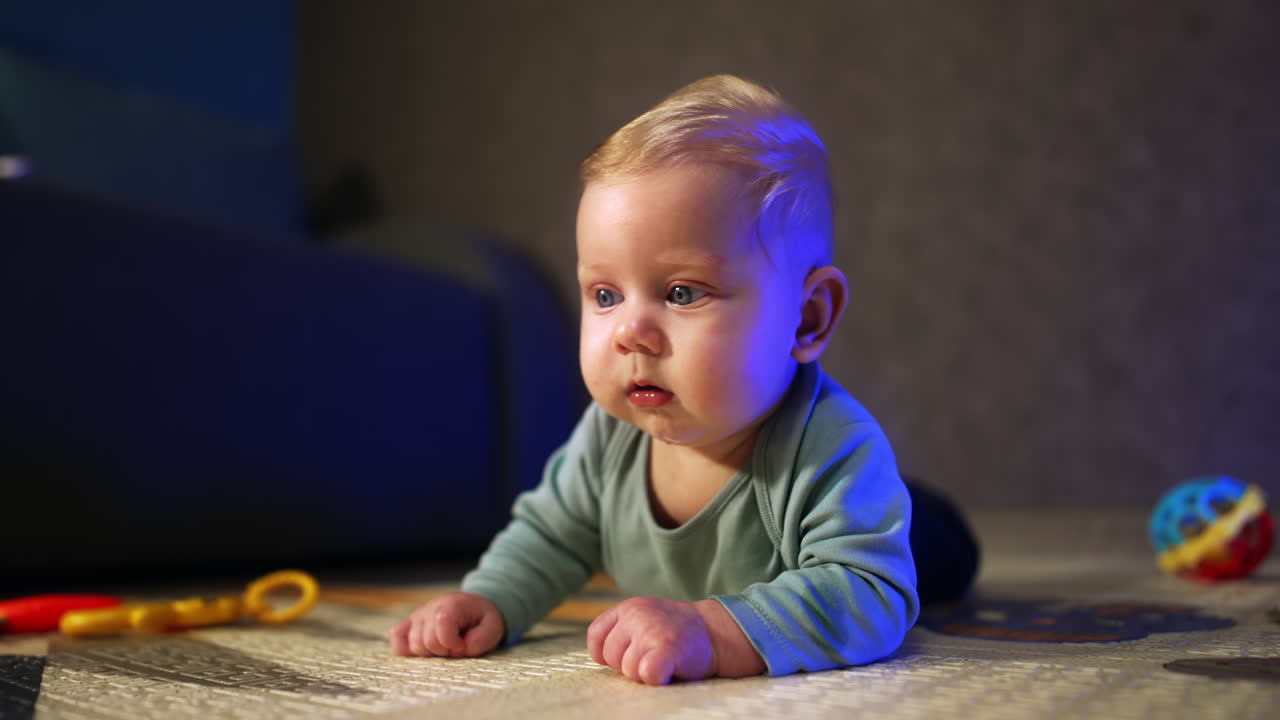 Cute tiny infant looking around with surprise. Adorable kid lies on his belly in front of camera. Close up.