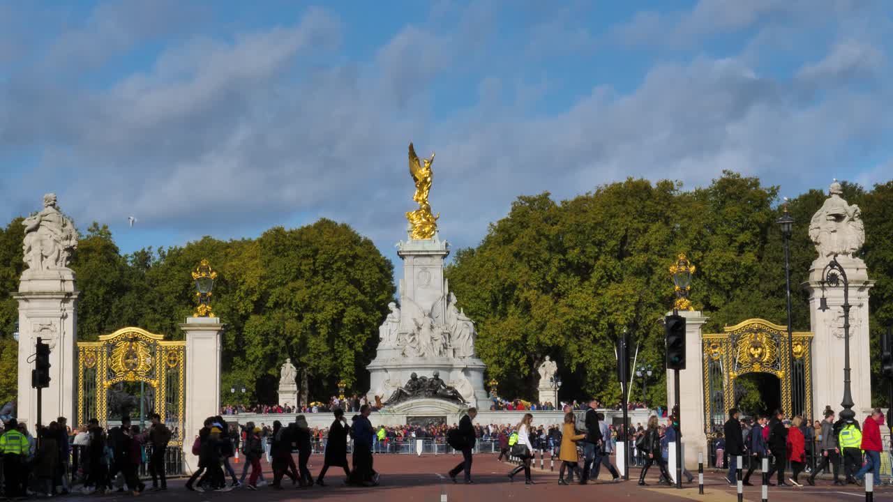 People crossing a busy street beneath the iconic Victoria Memorial: a golden statue in front of Buckingham Palace, in the City of Westminster in Central London, UK.