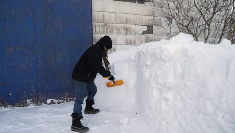 man shoveling snow off snowbank in front of a barn