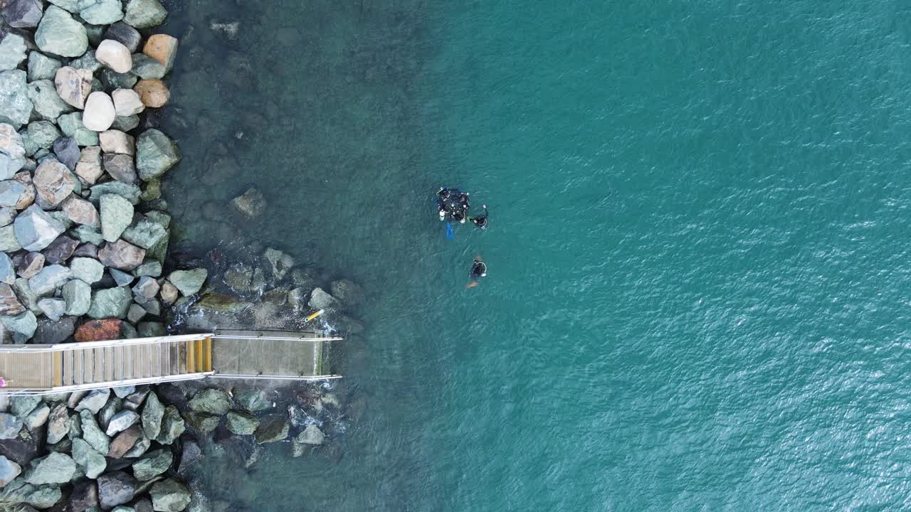 스쿠버 다이버 그룹이 바다로 이어지는 계단 근처 물 위에 모입니다.