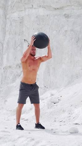 an athletic male strongman does exercises with a fitness ball to strengthen muscles. outdoor activities. vertical video