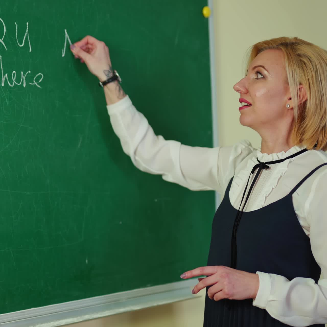 Education concept. Beautiful teacher writes on a blackboard. Creative female teacher standing near the chalkboard and writing with white chalk.