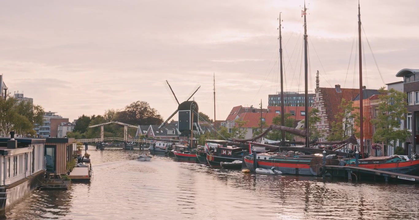 Porto storico a Leida, Paesi Bassi, Europa, con barche tradizionali, un mulino a vento e un ponte levatoio sotto un caldo cielo al tramonto