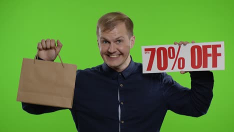 쇼핑 가방과 70%까지 할인 된 문장 표지판을 보여주는 행복한 남자.