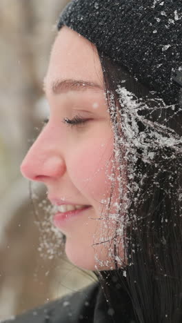primer plano de una mujer joven con gorra negra con copos de nieve en el cabello y la chaqueta, mirando hacia arriba con una cálida sonrisa antes de mirar hacia otro lado, capturando un momento contemplativo en medio de la nieve suave que cae