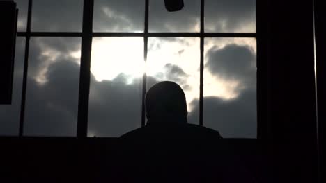 silhouette of business man walking up escalator in front of big window panels with clouds and sun