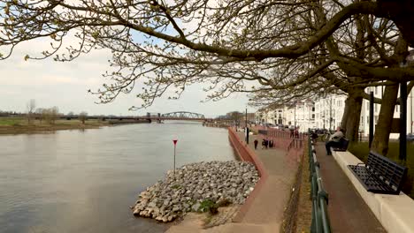 time lapse showing people strolling by and relaxing along the river ijssel embankment of hanseatic dutch city zutphen with water and cargo ship passing by