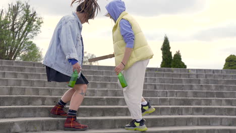 Two-Urban-Girls-Sitting-On-Stairs-With-Beer-Bottles-And-Pizza-Box