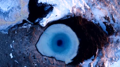 aerial view of a drone which getting further and further of the center of a geuser in geysir, iceland . smoke is getting out of the geyser with people walking all around the geyser, under the red sunset.