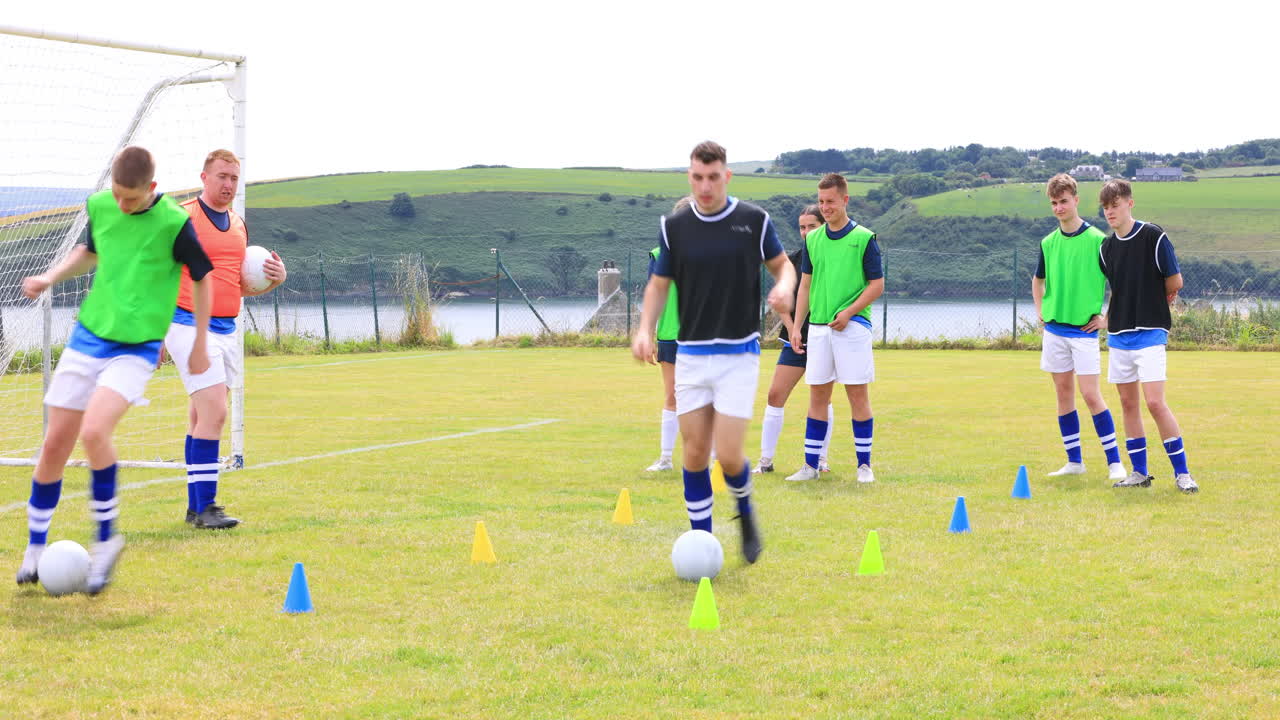Male and female soccer players running after ball and avoiding cones with coach on pitch