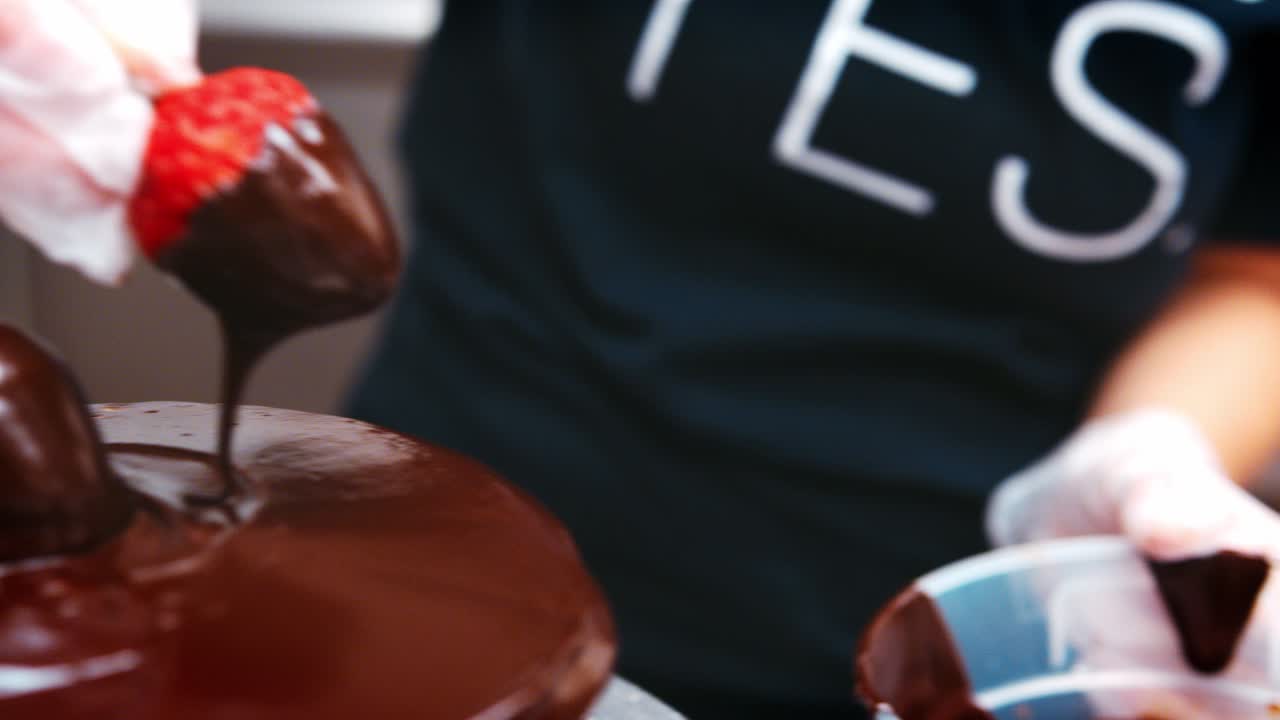 Pasticcere che intinge fragole nel cioccolato per la decorazione di torte.