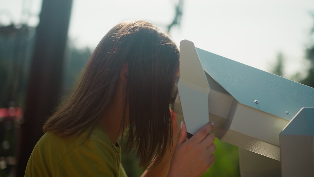 집중된 여성은 이동하는 케이블카에 대항하여 관측 갑판에 설치된 관광 안경을 통해 시야를 즐기고 있습니다.