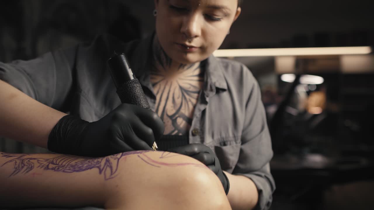 Donna caucasica concentrata che tatua le braccia del suo cliente.