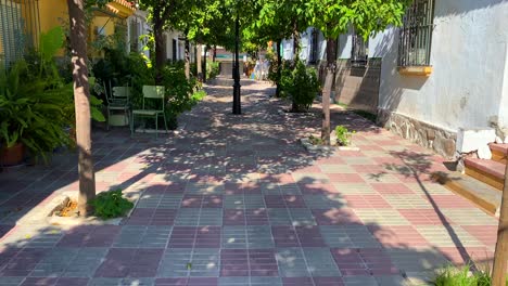 Orange-trees-in-a-typical-little-narrow-Spanish-street-with-houses-in-Marbella-old-town-Spain,-sunny-day-and-blue-sky,-4K-tilting-up