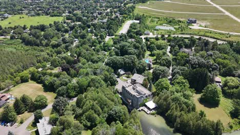 flyover of millcroft inn showing rooftop, forest border, and walkways on lush summer grounds