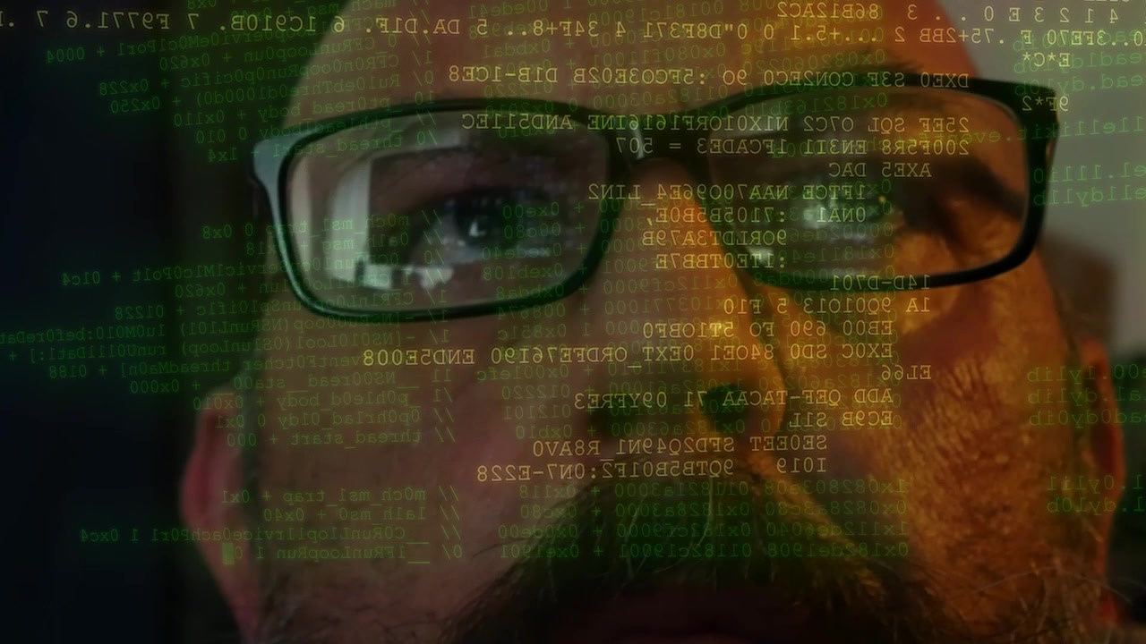 Mann mit Brille, der Codezeilen und angezeigte Daten vor seinem Gesicht durchsucht.