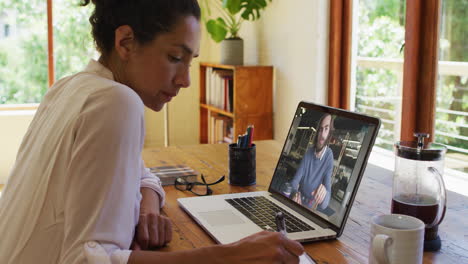 african american woman taking notes while having a video call on laptop at home