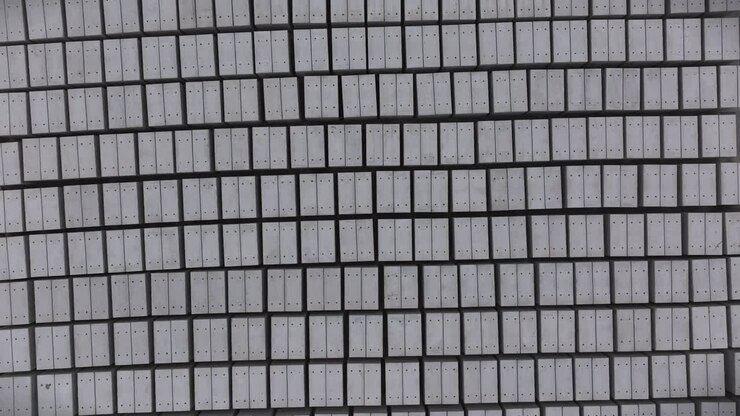 Top-down Aerial View of precision-engineered grid of uniform gray rectangular concrete panels, meticulously aligned in a systematic pattern with subtle depth and architectural symmetry.