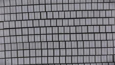top-down aerial view of precision-engineered grid of uniform gray rectangular concrete panels, meticulously aligned in a systematic pattern with subtle depth and architectural symmetry.