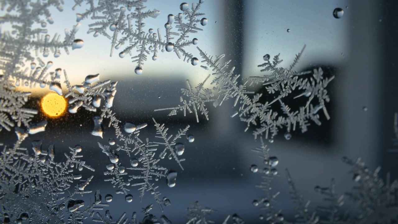 Visar frostkristaller som skimrar på ett glasfönster hemma, med låg sol som flyttar och ändrar dropparna