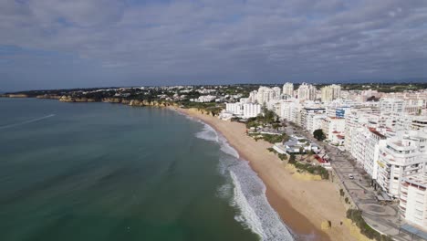 tomada aérea del frente del mar de los edificios de armação de pera, la playa de arena y el paseo marítimo, algarve