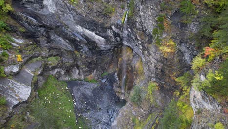 Waterfall-on-paradise-landscape-with-Autumn-colors-and-beautiful-rocks,-sheep-graze-on-Alpine-meadow