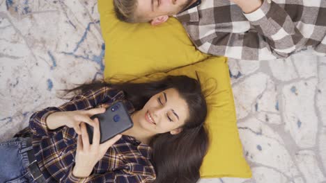 Happy-young-lovers-looking-at-their-phones-lying-on-the-floor.