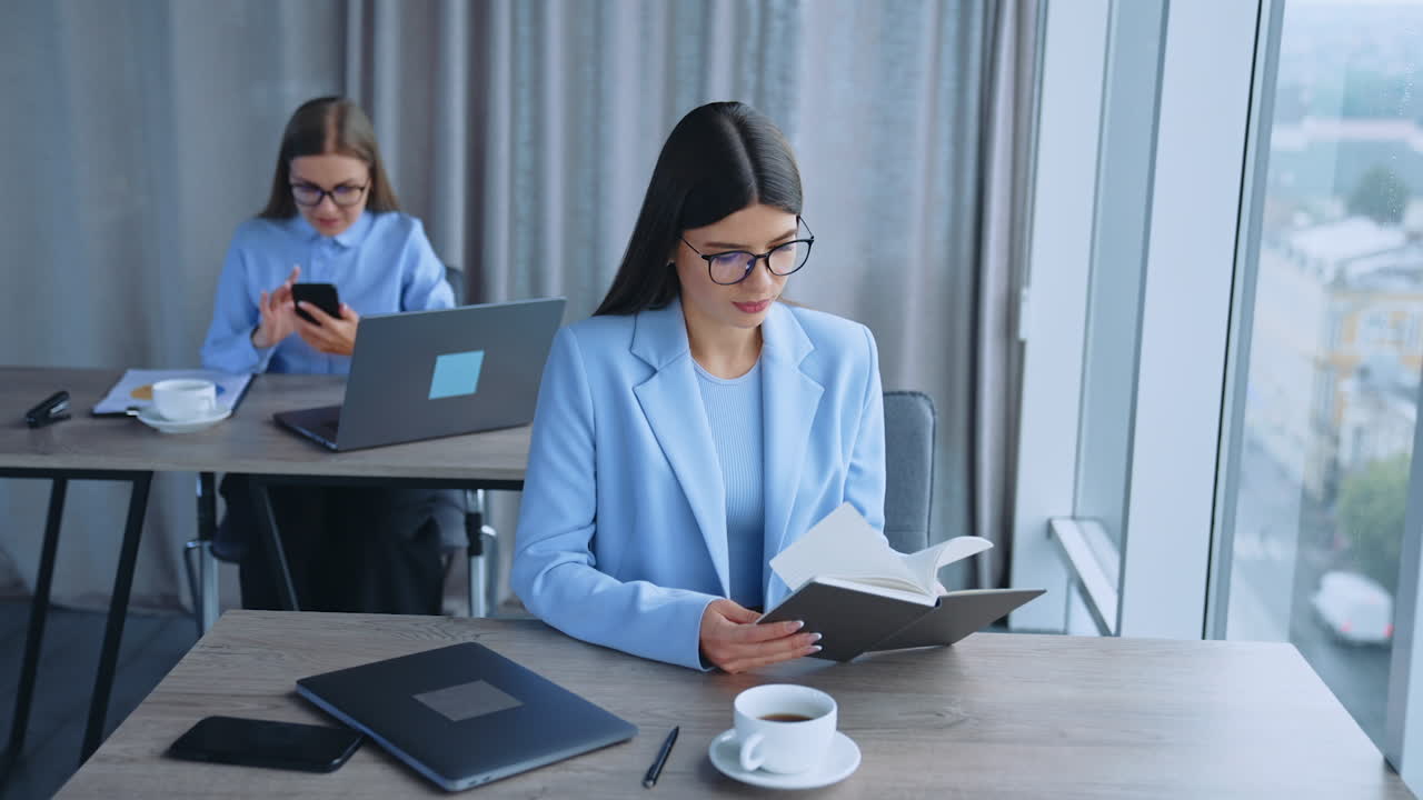 Busy female office employees in the light modern room. Ladies sitting at desks wearing glasses looking into camera.