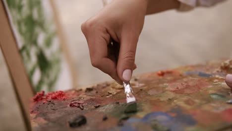 close up of a artist female's hand mixing paints on palette and applies it on her surface on easel. working process. outdoors