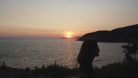 Girl-walking-along-a-cliff-by-the-sea-on-sunset,-golden-hour