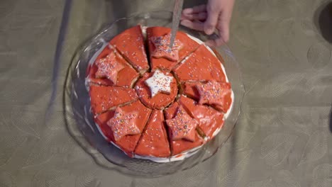 una mujer corta un pastel decorado con crema y glaseado rojo en partes iguales con un gran cuchillo de cocina. el concepto de una fiesta familiar. primer plano. vista superior. 4k.
