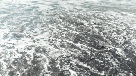 dynamic foam textures on black pebble beach, as waves roll in and out