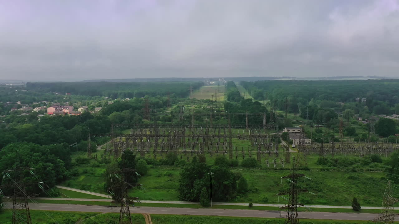 High voltage steel power station. Flight over power transmission lines in green field countryside. Electric tower line in a summer day. Aerial view.